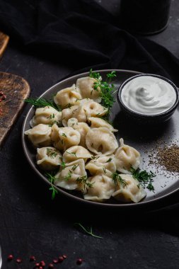 Ekşi kremalı hamur tatlısı ve siyah tabakta otlar. Etli börek.