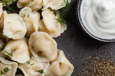 Ekşi kremalı hamur tatlısı ve siyah tabakta otlar. Etli börek.