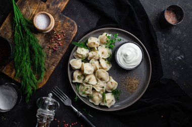 Ekşi kremalı hamur tatlısı ve siyah tabakta otlar. Etli börek.