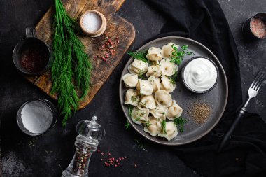 Ekşi kremalı hamur tatlısı ve siyah tabakta otlar. Etli börek.