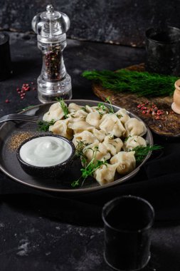 Ekşi kremalı hamur tatlısı ve siyah tabakta otlar. Etli börek.