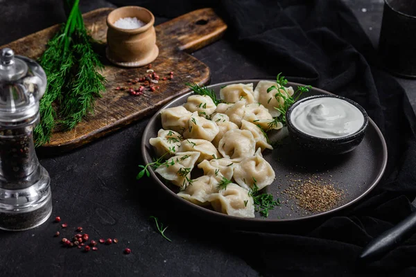 stock image Dumplings with sour cream and herbs on a dark plate. Meat dumplings