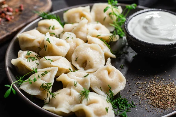 stock image Dumplings with sour cream and herbs on a dark plate. Meat dumplings