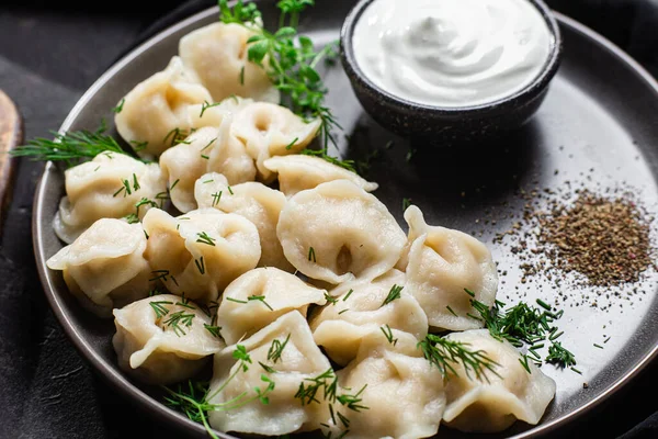 stock image Dumplings with sour cream and herbs on a dark plate. Meat dumplings