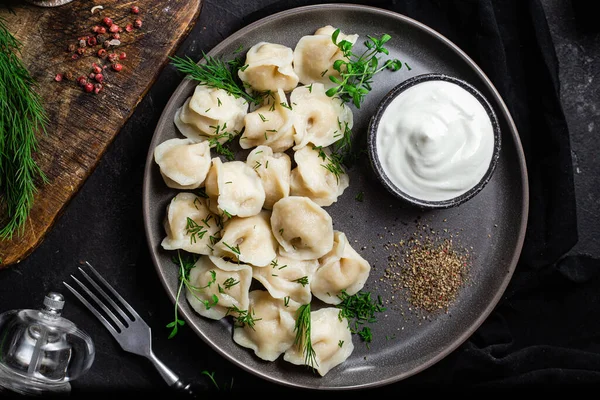 Ekşi kremalı hamur tatlısı ve siyah tabakta otlar. Etli börek.