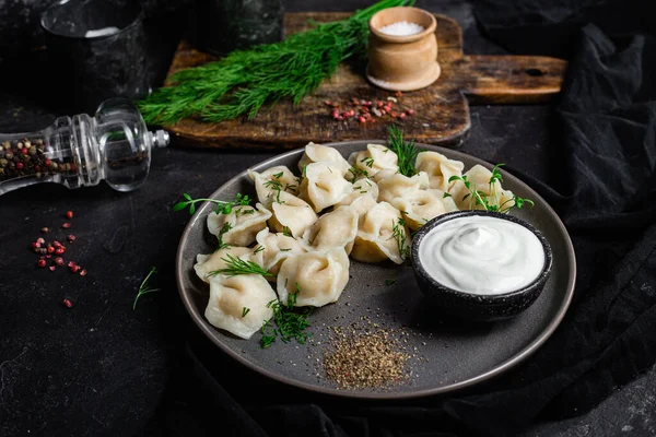 Ekşi kremalı hamur tatlısı ve siyah tabakta otlar. Etli börek.