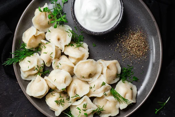 Ekşi kremalı hamur tatlısı ve siyah tabakta otlar. Etli börek.