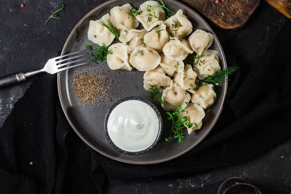 stock image Dumplings with sour cream and herbs on a dark plate. Meat dumplings