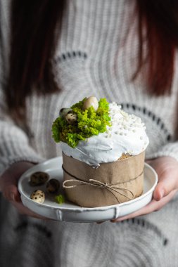 Bir kadın elinde kremalı Paskalya pastası ve bir tabakta dekor tutuyor.