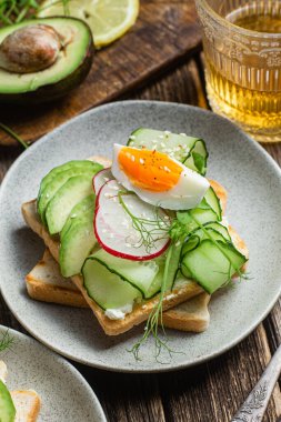 White bread toasts with cream cheese, egg, avocado, cucumber and radish in a plate clipart