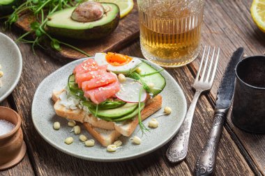 Krem peynirli beyaz ekmek tostları, somon, yumurta, avokado, salatalık ve turp tabakta.