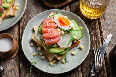 Krem peynirli beyaz ekmek tostları, somon, yumurta, avokado, salatalık ve turp tabakta.
