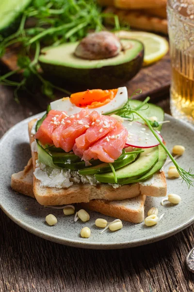 Krem peynirli beyaz ekmek tostları, somon, yumurta, avokado, salatalık ve turp tabakta.