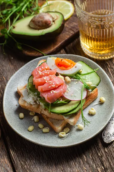 Krem peynirli beyaz ekmek tostları, somon, yumurta, avokado, salatalık ve turp tabakta.