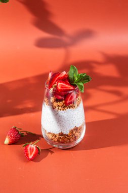 Yoğurtlu granola, chia ve çilekli parlak bir arka planda bir bardak