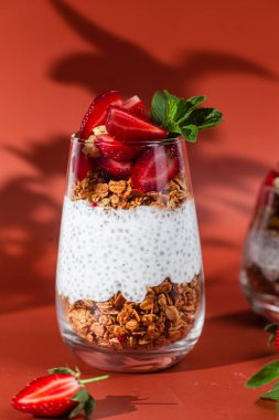 Yoğurtlu granola, chia ve çilekli parlak bir arka planda bir bardak