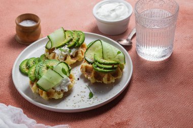 Krem peynirli waffle, bir tabakta avokado ve salatalık