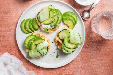 Krem peynirli waffle, bir tabakta avokado ve salatalık