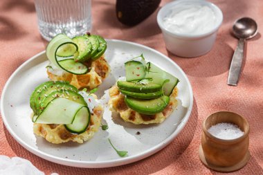 Krem peynirli waffle, bir tabakta avokado ve salatalık