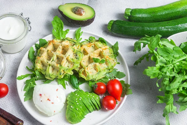 Zucchini waffles, poached egg, avocado and cherry tomatoes in a plate