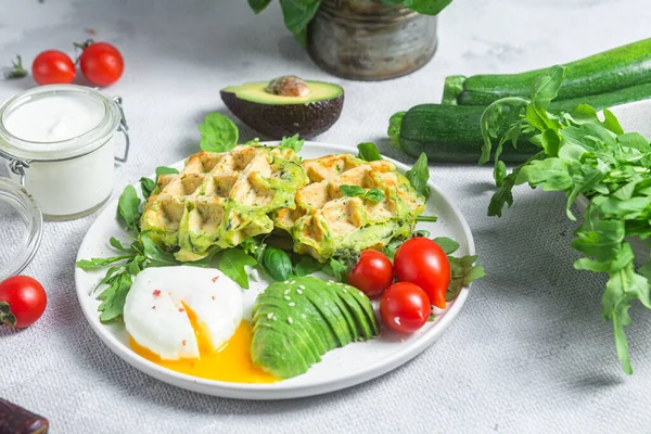 Zucchini waffles, poached egg, avocado and cherry tomatoes in a plate