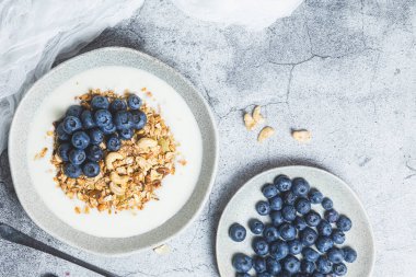 Yoğurtlu granola ve gri arka planda bir tabakta yabanmersini.