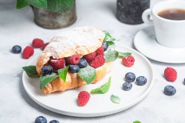 Beyaz tabakta ahududu, yaban mersini ve krem peynirli kruvasan.