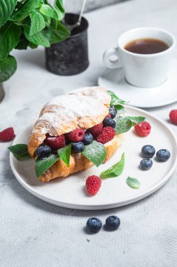 Beyaz tabakta ahududu, yaban mersini ve krem peynirli kruvasan.