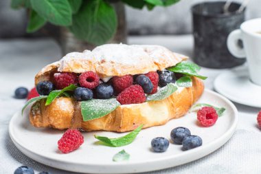 Beyaz tabakta ahududu, yaban mersini ve krem peynirli kruvasan.