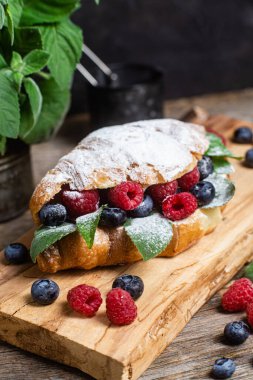 Tahtada ahududu, yaban mersini ve krem peynirli kruvasan.