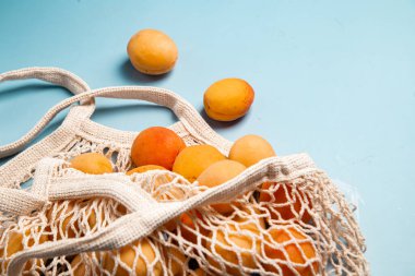 Parlak bir arka planda, ekolojik bir çantada kayısı. Satın Al