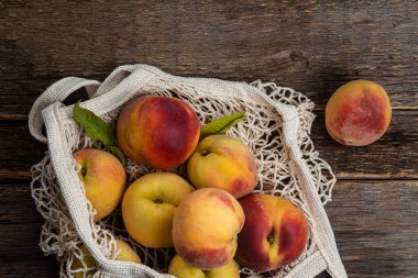 Olgun şeftaliler ahşap arka planda, eko torba içinde.