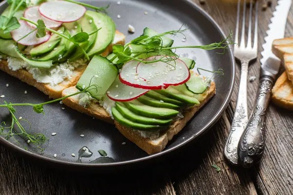 White bread toasts with cream cheese, avocado, cucumber and radish in a plate