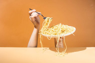 Masadaki beyaz tabakta spagetti yiyen bir kız.