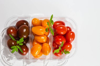 Açık arkaplanda farklı renklerde domatesler. Plastik bir kabın içindeki domatesler