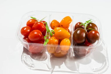 Açık arkaplanda farklı renklerde domatesler. Plastik bir kabın içindeki domatesler