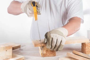 Yakından testereyle tahta kiriş kesen bir adam.