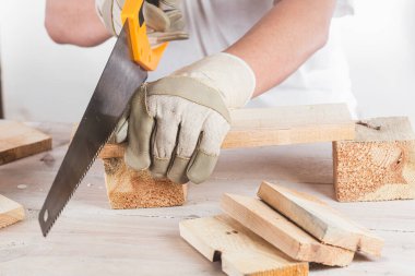 Yakından testereyle tahta kiriş kesen bir adam.