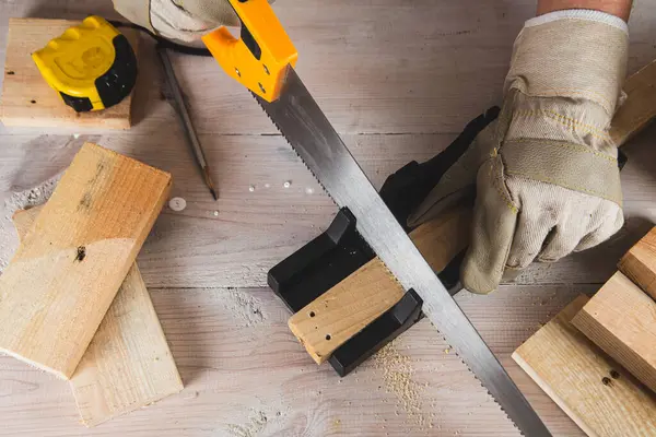 Yakından testereyle tahta kiriş kesen bir adam.