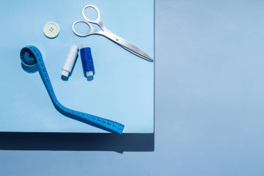 Aksesuar dikiyorum. İplikler, makas, mezura, mavi arkaplandaki düğmeler