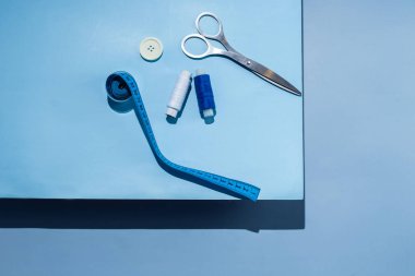 Aksesuar dikiyorum. İplikler, makas, mezura, mavi arkaplandaki düğmeler