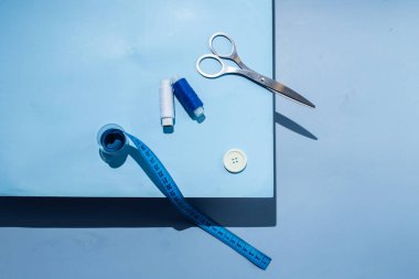Aksesuar dikiyorum. İplikler, makas, mezura, mavi arkaplandaki düğmeler