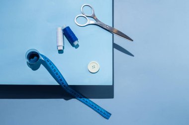Aksesuar dikiyorum. İplikler, makas, mezura, mavi arkaplandaki düğmeler