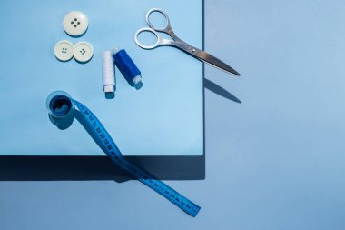 Aksesuar dikiyorum. İplikler, makas, mezura, mavi arkaplandaki düğmeler