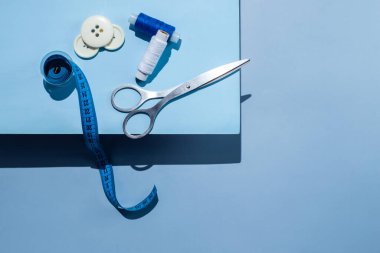 Aksesuar dikiyorum. İplikler, makas, mezura, mavi arkaplandaki düğmeler