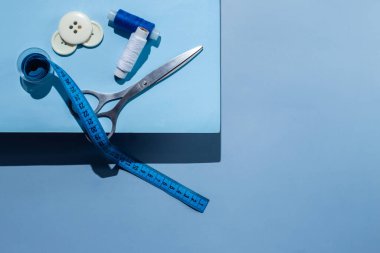 Aksesuar dikiyorum. İplikler, makas, mezura, mavi arkaplandaki düğmeler