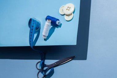 Aksesuar dikiyorum. İplikler, makas, mezura, mavi arkaplandaki düğmeler