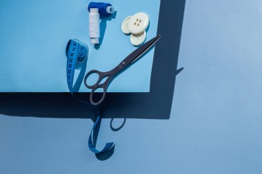 Aksesuar dikiyorum. İplikler, makas, mezura, mavi arkaplandaki düğmeler