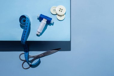 Aksesuar dikiyorum. İplikler, makas, mezura, mavi arkaplandaki düğmeler