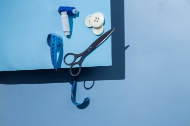 Aksesuar dikiyorum. İplikler, makas, mezura, mavi arkaplandaki düğmeler